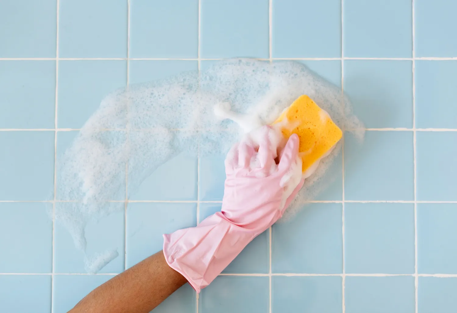 backsplash tiles cleaning – karpet king design center person wearing a pink rubber glove scrubs light blue tiled wall with a yellow sponge and sudsy foam.